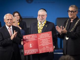 Im Vordergrund sind drei Personen zu sehen: links Vorsitzender des Karlspreisdirektoriums Dr. Jürgen Linden, in der Mitte Karlspreisträger 2024 Oberrabbiner Pinchas Goldschmidt, rechts Sibylle Keupen Oberbürgermeisterin der Stadt Aachen